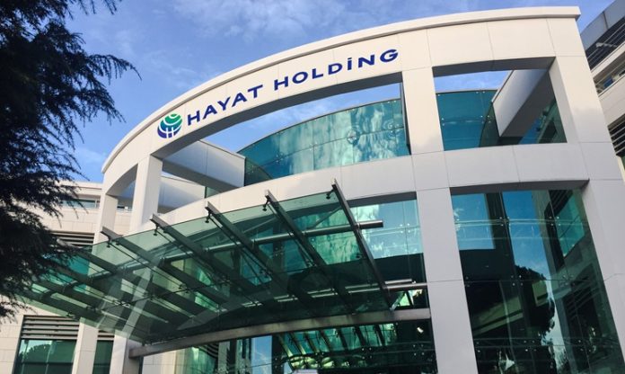 Hayat Holding Türkiye’nin en büyük sanayi gruplarından biri olan Hayat Holding, hızlı tüketim ürünlerinden liman işletmeciliğine, ahşap panel üretiminden enerji yatırımlarına kadar uzanan geniş faaliyet ağıyla dikkat çekiyor. 1937 yılında temelleri atılan grup, bugün dünyanın farklı bölgelerinde üretim yapan küresel bir holding yapısına dönüşmüş durumda. Özellikle temizlik kağıtları, hijyen ürünleri ve yapı malzemeleri alanındaki yatırımlarıyla öne çıkan Hayat Holding, Türkiye merkezli en büyük uluslararası üretim şirketleri arasında gösteriliyor. Konulu bir haber görseli.